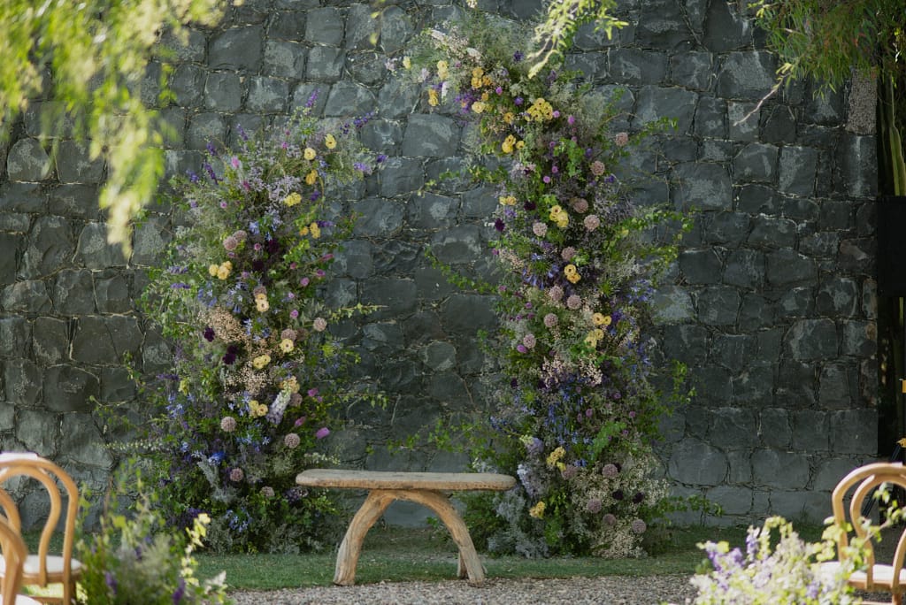 Romantic garden-style wedding flowers featuring mauve, blush, plum, and buttery yellow blooms styled by a wedding florist in San Miguel de Allende, Mexico. The bouquet and floral centerpiece include lisianthus, ranunculus, and delicate filler flowers, perfect for an elegant destination wedding. Captured at Casa Adela with soft candlelight and seasonal fruits, the floral design blends old-world charm with modern romance.
