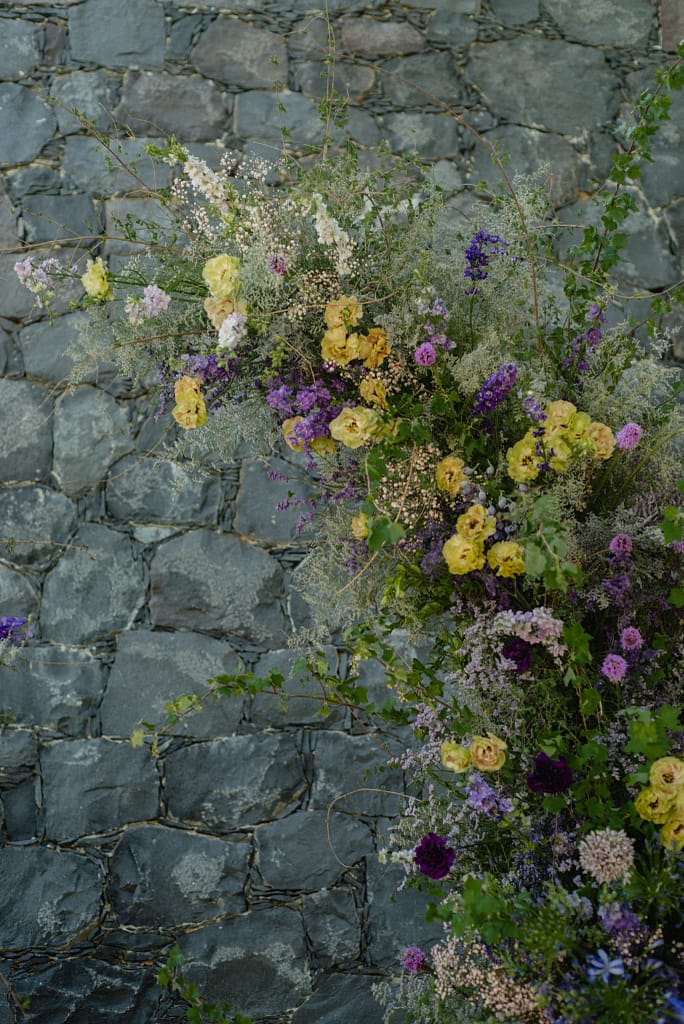 Romantic garden-style wedding flowers featuring mauve, blush, plum, and buttery yellow blooms styled by a wedding florist in San Miguel de Allende, Mexico. The bouquet and floral centerpiece include lisianthus, ranunculus, and delicate filler flowers, perfect for an elegant destination wedding. Captured at Casa Adela with soft candlelight and seasonal fruits, the floral design blends old-world charm with modern romance.