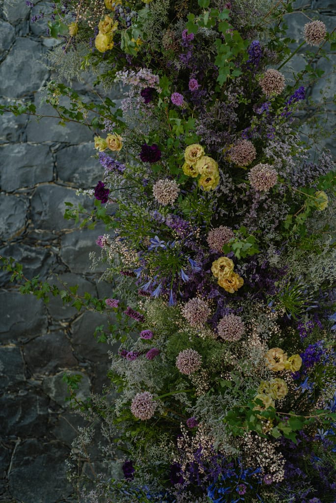 Romantic garden-style wedding flowers featuring mauve, blush, plum, and buttery yellow blooms styled by a wedding florist in San Miguel de Allende, Mexico. The bouquet and floral centerpiece include lisianthus, ranunculus, and delicate filler flowers, perfect for an elegant destination wedding. Captured at Casa Adela with soft candlelight and seasonal fruits, the floral design blends old-world charm with modern romance.