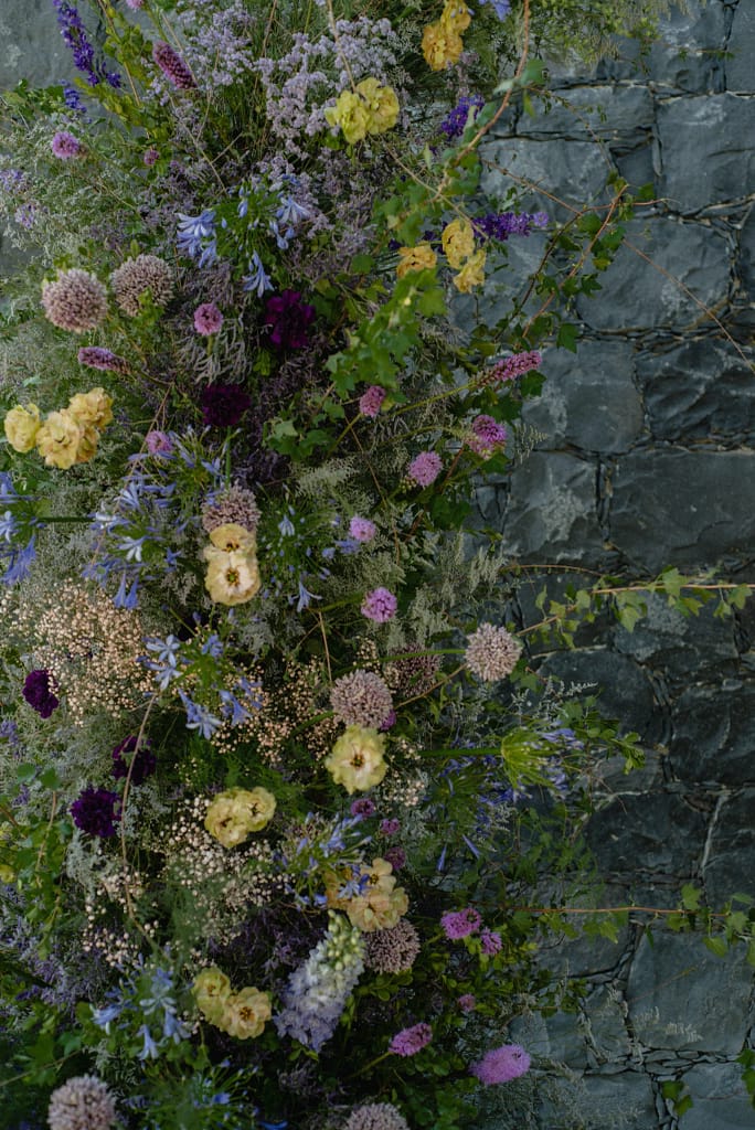 Romantic garden-style wedding flowers featuring mauve, blush, plum, and buttery yellow blooms styled by a wedding florist in San Miguel de Allende, Mexico. The bouquet and floral centerpiece include lisianthus, ranunculus, and delicate filler flowers, perfect for an elegant destination wedding. Captured at Casa Adela with soft candlelight and seasonal fruits, the floral design blends old-world charm with modern romance.